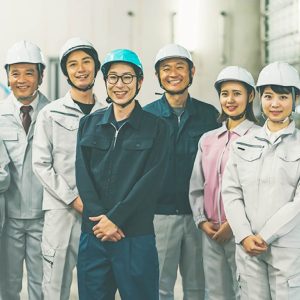 ヘルメットと作業服をきた男女5名が笑顔で立っている写真