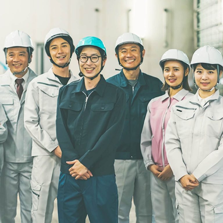 ヘルメットと作業服をきた男女5名が笑顔で立っている写真